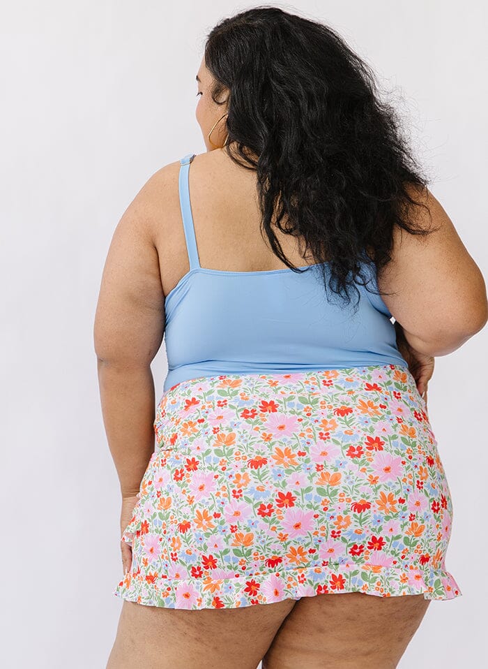 Photo of a woman wearing a floral swim skirt bottom and a blue swim top back angle